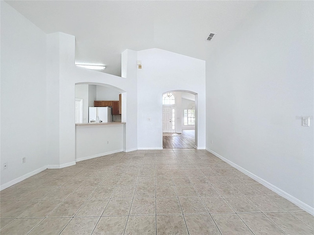 unfurnished living room with visible vents, high vaulted ceiling, arched walkways, light tile patterned floors, and baseboards