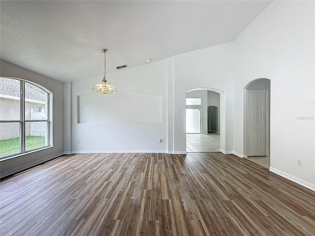 empty room with arched walkways, visible vents, baseboards, and wood finished floors