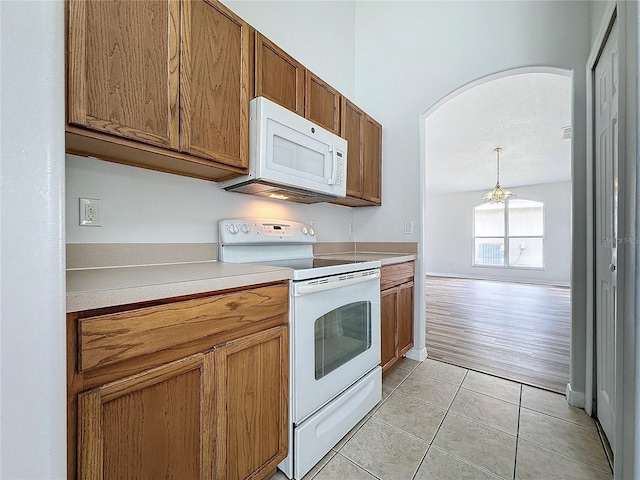 kitchen with light tile patterned floors, white appliances, brown cabinetry, and arched walkways