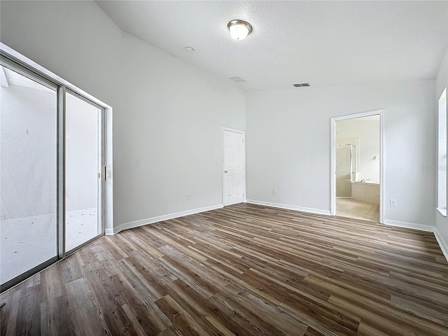 unfurnished bedroom with wood finished floors, visible vents, baseboards, lofted ceiling, and connected bathroom