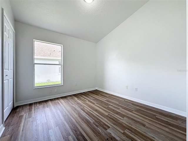 spare room with baseboards, dark wood-style flooring, and vaulted ceiling