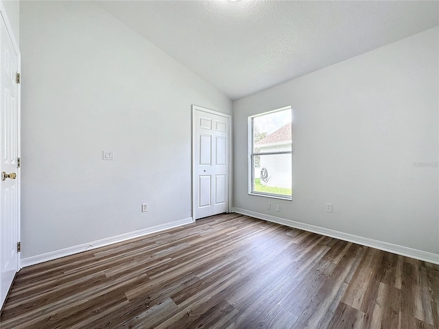 unfurnished bedroom with vaulted ceiling, baseboards, dark wood-style flooring, and a closet