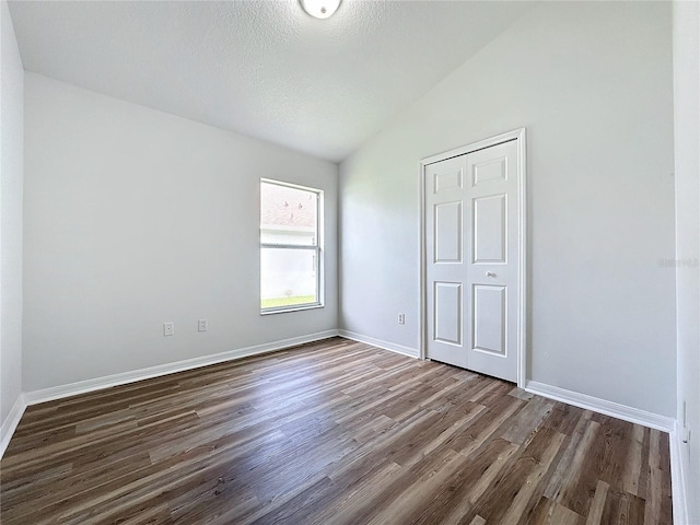 unfurnished bedroom featuring vaulted ceiling, wood finished floors, baseboards, and a textured ceiling