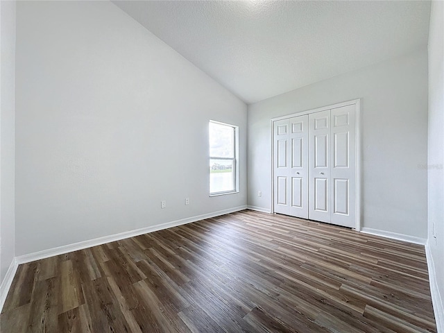 unfurnished bedroom featuring lofted ceiling, baseboards, dark wood-style flooring, and a closet