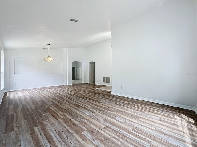 unfurnished living room featuring wood finished floors, arched walkways, visible vents, and baseboards