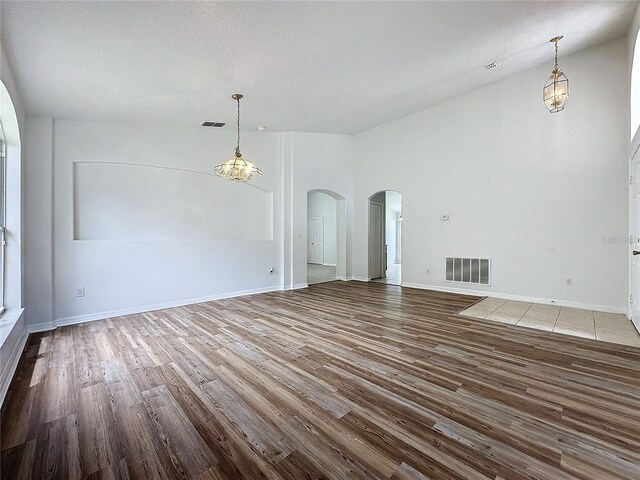 unfurnished living room with wood finished floors, arched walkways, visible vents, and baseboards