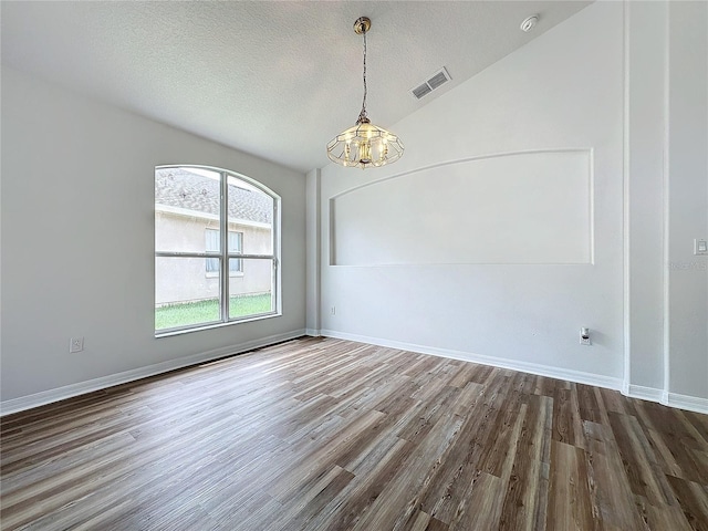 empty room featuring a textured ceiling, wood finished floors, baseboards, a chandelier, and vaulted ceiling