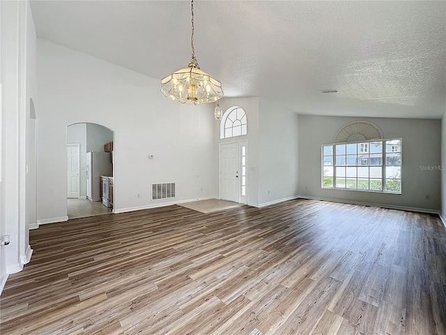 interior space with visible vents, baseboards, wood finished floors, arched walkways, and a textured ceiling