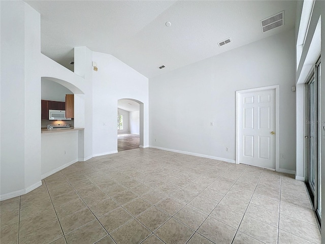 unfurnished room with light tile patterned floors, visible vents, baseboards, and high vaulted ceiling