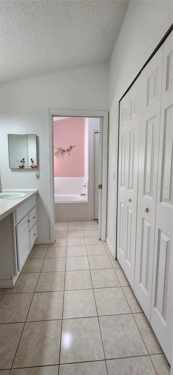 bathroom featuring tile patterned flooring, a textured ceiling, tiled bath, and vanity