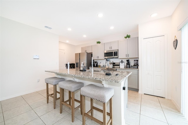 kitchen featuring a center island with sink, light stone counters, appliances with stainless steel finishes, and light tile patterned flooring