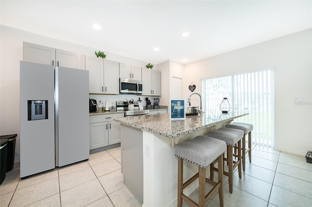 kitchen featuring a kitchen breakfast bar, an island with sink, stainless steel appliances, light stone counters, and light tile patterned flooring