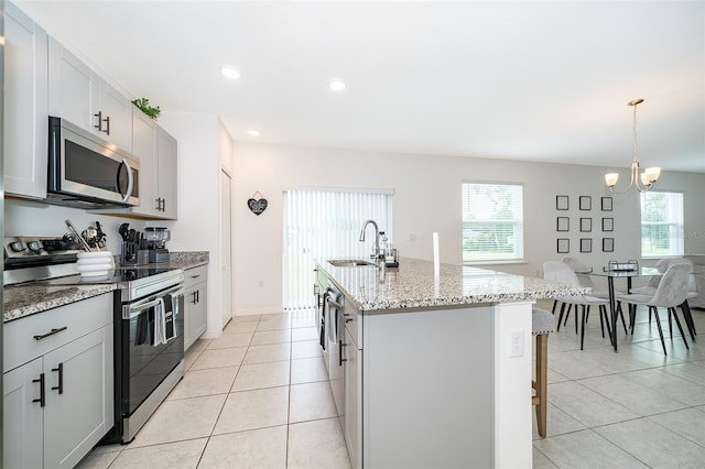 kitchen with a kitchen island with sink, pendant lighting, stainless steel appliances, sink, and a breakfast bar area