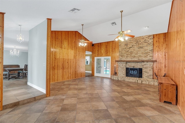 living room featuring high vaulted ceiling, ceiling fan with notable chandelier, wooden walls, and a brick fireplace