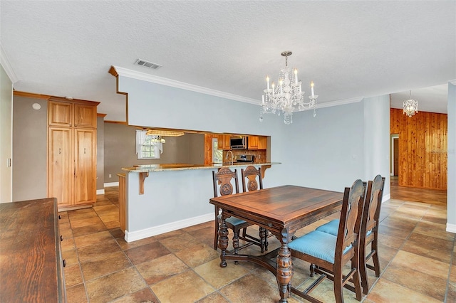 dining room with a textured ceiling, an inviting chandelier, ornamental molding, sink, and wooden walls