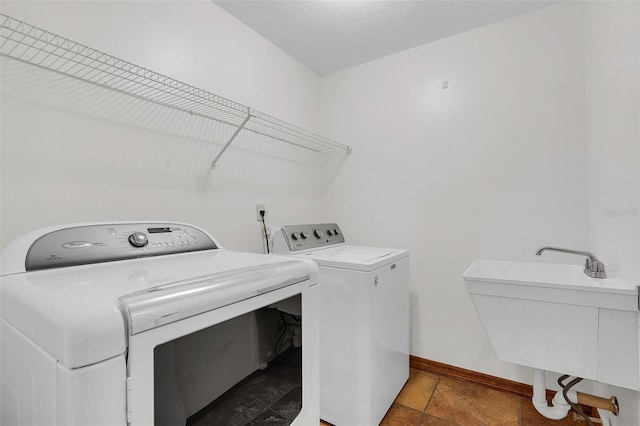 clothes washing area with a textured ceiling, washing machine and dryer, and sink