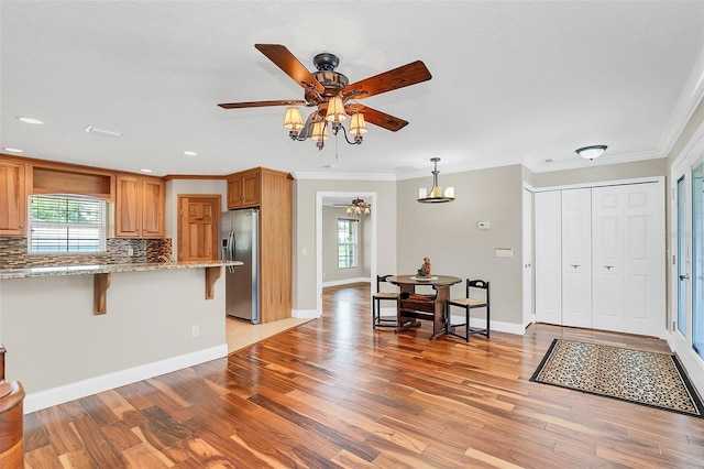 kitchen with stainless steel refrigerator with ice dispenser, light hardwood / wood-style floors, a breakfast bar, kitchen peninsula, and ceiling fan