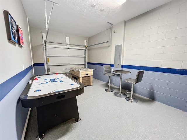 rec room with speckled floor, concrete block wall, a garage, and a textured ceiling