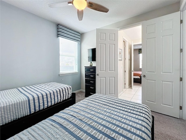 bedroom featuring light carpet, a ceiling fan, a textured ceiling, light tile patterned flooring, and baseboards