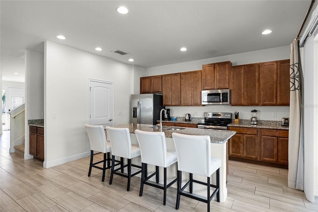 kitchen with appliances with stainless steel finishes, light stone countertops, sink, an island with sink, and a breakfast bar area