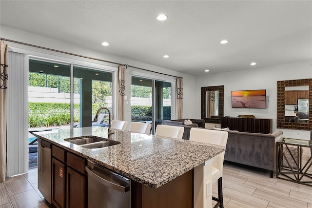 kitchen featuring light stone countertops, stainless steel appliances, a kitchen island with sink, sink, and dark brown cabinetry