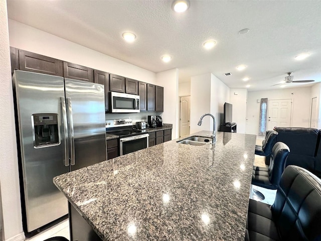 kitchen with a textured ceiling, dark brown cabinets, stainless steel appliances, sink, and ceiling fan