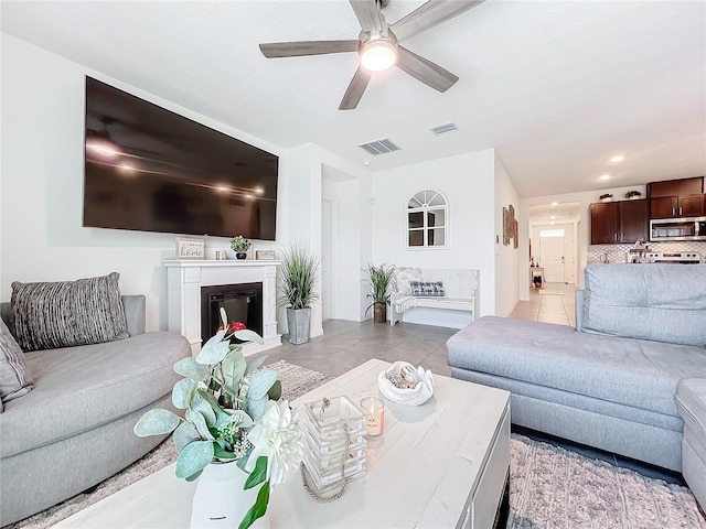living area with ceiling fan, visible vents, a glass covered fireplace, and light tile patterned floors
