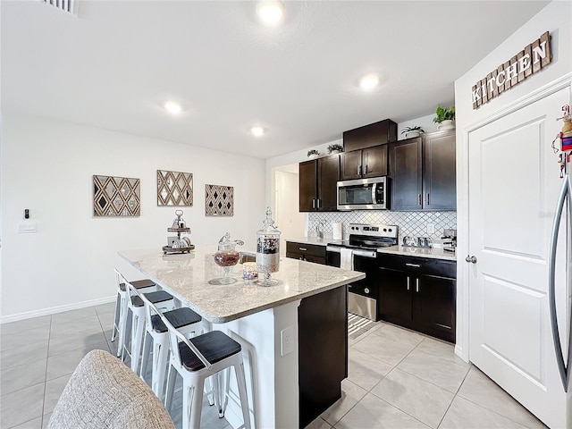 kitchen with a center island, a kitchen bar, dark brown cabinetry, appliances with stainless steel finishes, and light stone counters