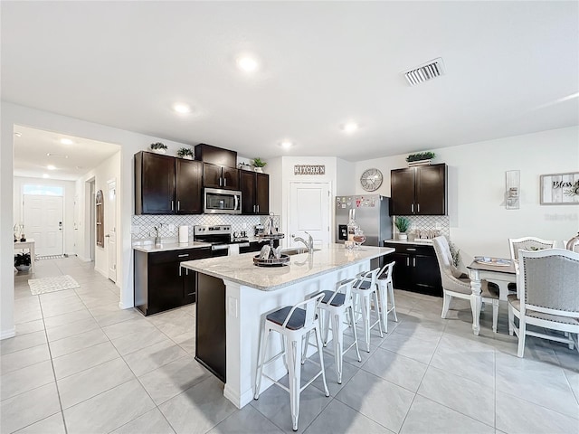 kitchen with backsplash, a kitchen island with sink, a kitchen bar, sink, and stainless steel appliances