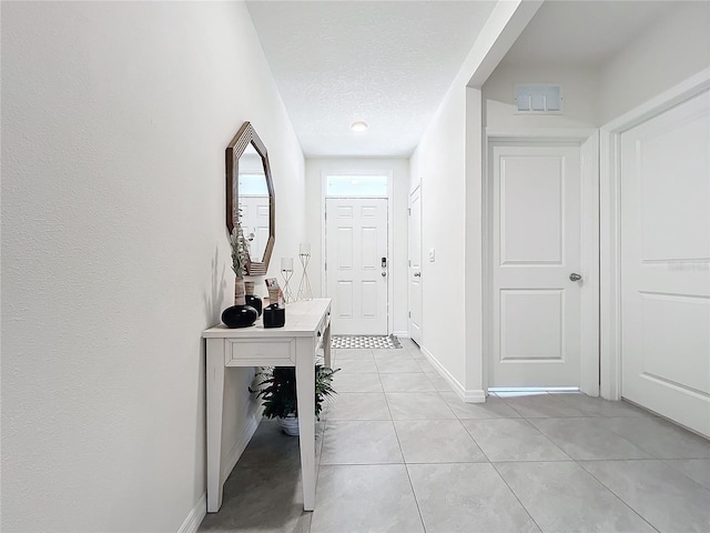 hallway with baseboards, a textured ceiling, and light tile patterned flooring