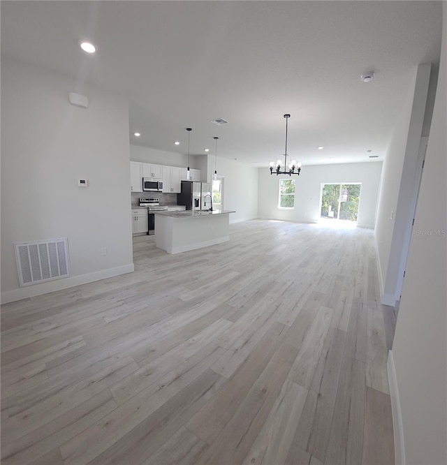 unfurnished living room featuring light wood-type flooring, sink, and a notable chandelier