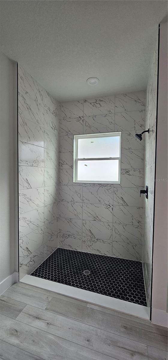 bathroom with a textured ceiling, wood-type flooring, and tiled shower