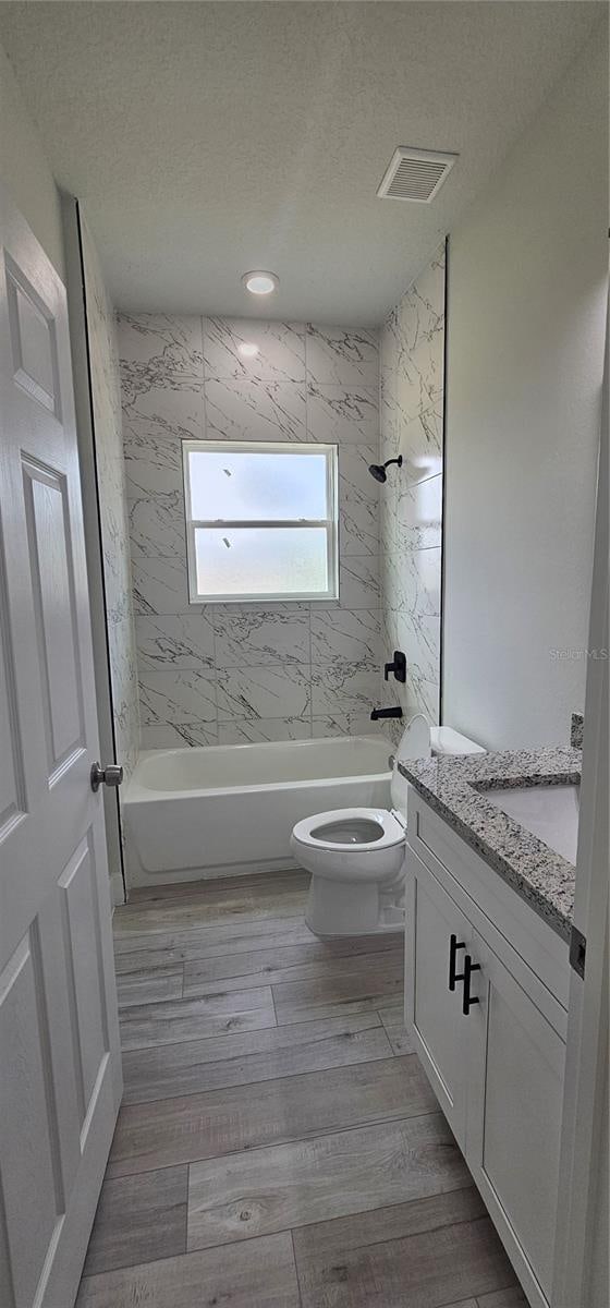 full bathroom with toilet, vanity, a textured ceiling, tiled shower / bath combo, and hardwood / wood-style flooring