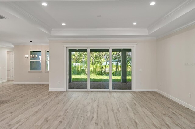 empty room with a chandelier, light hardwood / wood-style floors, a tray ceiling, and crown molding