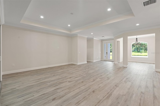 unfurnished living room with ornamental molding, a tray ceiling, light hardwood / wood-style floors, and a notable chandelier