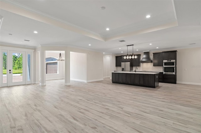 kitchen with an island with sink, stainless steel appliances, light hardwood / wood-style flooring, and custom range hood