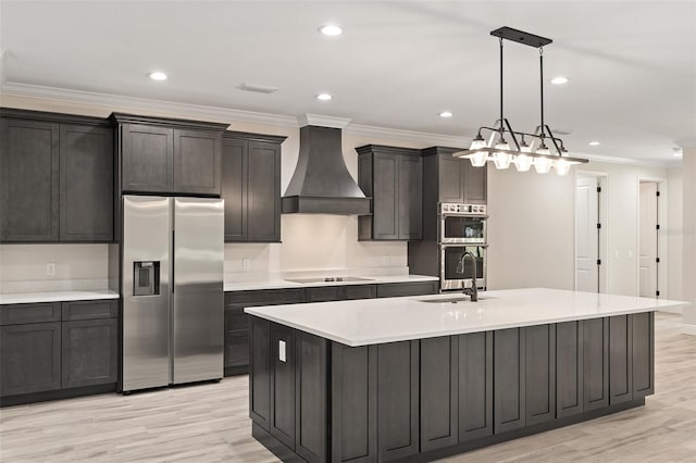 kitchen with appliances with stainless steel finishes, light hardwood / wood-style flooring, premium range hood, a kitchen island with sink, and sink