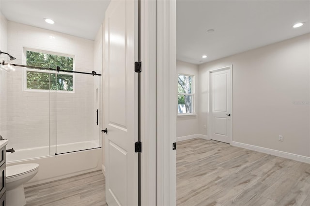 full bathroom with wood-type flooring, combined bath / shower with glass door, toilet, and a healthy amount of sunlight