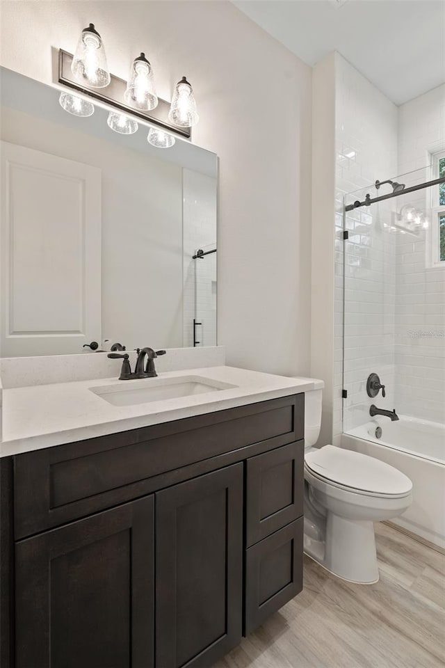 full bathroom with wood-type flooring, tiled shower / bath, vanity, and toilet