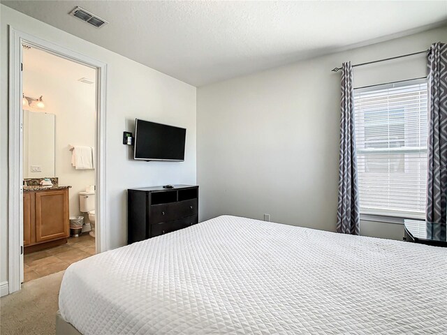 carpeted bedroom featuring a textured ceiling and ensuite bathroom