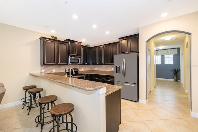 kitchen with backsplash, appliances with stainless steel finishes, a kitchen bar, kitchen peninsula, and light stone counters