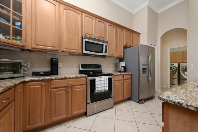 kitchen featuring crown molding, washer and dryer, light stone countertops, appliances with stainless steel finishes, and light tile patterned flooring