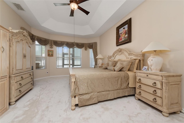 bedroom with ceiling fan, light colored carpet, and a raised ceiling