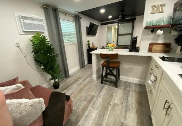 kitchen with light hardwood / wood-style floors, white cabinetry, kitchen peninsula, a kitchen bar, and black electric stovetop