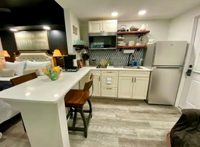 kitchen featuring light hardwood / wood-style floors, tasteful backsplash, stainless steel refrigerator, a breakfast bar area, and sink