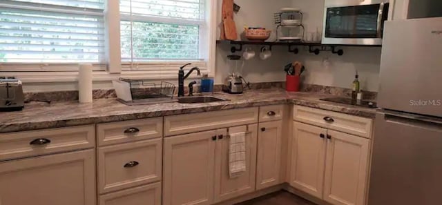 kitchen with light stone counters, appliances with stainless steel finishes, sink, and white cabinetry