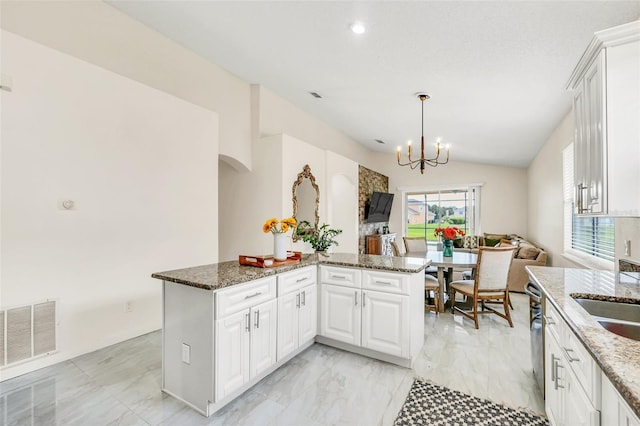 kitchen with kitchen peninsula, vaulted ceiling, dark stone countertops, white cabinets, and hanging light fixtures