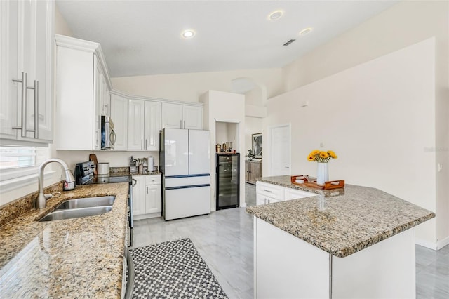 kitchen featuring white cabinets, stainless steel appliances, vaulted ceiling, and light stone counters