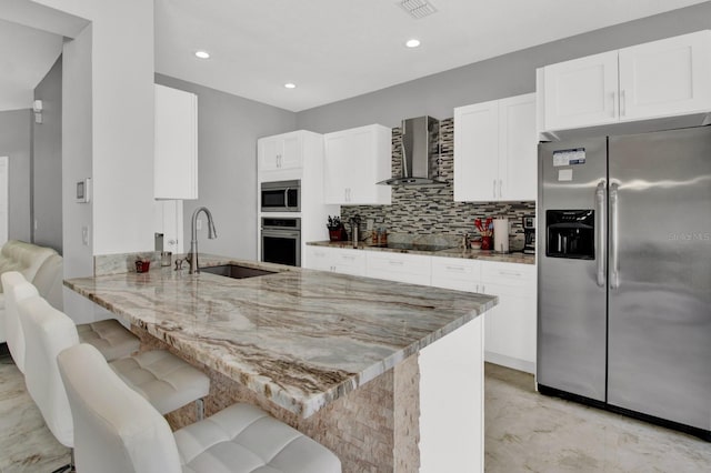 kitchen featuring kitchen peninsula, sink, wall chimney exhaust hood, stainless steel appliances, and a breakfast bar area