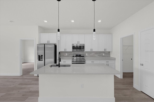 kitchen with an island with sink, sink, appliances with stainless steel finishes, and white cabinetry